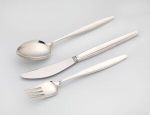  A set of silver tableware designed by Tias Eckhoff, including a reflective silver spoon, fork, and knife with minimalist design, displayed against a gentle grey background.