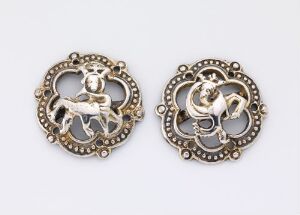  Antique style metallic pendants (or earrings) with intricate filigree borders featuring a cherub with wings on the left and a galloping horse on the right, both set against an off-white background.