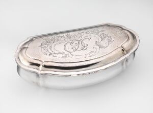  An elongated, oval-shaped silver container, titled "Dåse" by artist Jan Jansen Greve d.e., with polished surfaces and engraved floral scrollwork on the top, showcasing subtle contrasts of light reflecting on its curved edges.