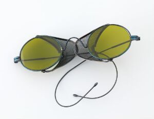  A pair of round, yellow-tinted sunglasses with thin, dark metal frames and a connecting cord, placed on a light gray background.