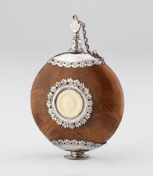  An ornate spherical object with a rich brown wood body and intricate silver metalwork, featuring a scalloped band around the middle, a circular lighter-colored inset, a decorative top finial with a small chain, and a metal stand at the base.