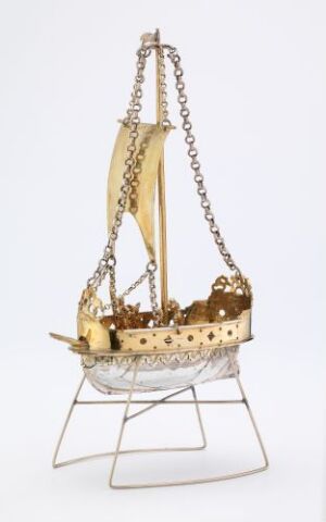  Ornamental golden sailing ship with intricate detailing, suspended by a chain from a silver wire stand against a white background. Artist name and title unknown.