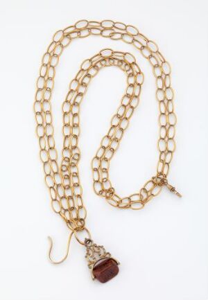  A gold necklace with interlinked round loops and a facetted, reddish-brown pendant on a plain, light background.