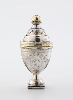  An ornate silver-toned vessel with elaborate etchings and a golden-hued band on a pedestal, against a plain light grey background.