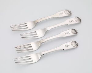  Four silver forks with decorative handles arranged diagonally on a light gray background.