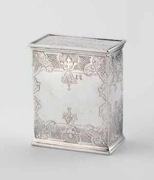  A rectangular forged silver tea caddy titled "Tedåse" by Gotlieb Middelthon, featuring intricate engravings of symmetrical floral designs and a less adorned central panel on the front, set against a neutral gray background.