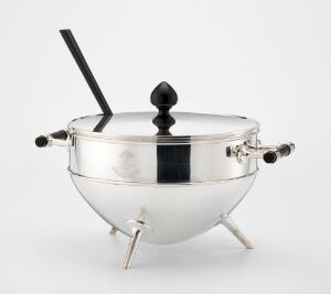  A reflective silver-plated serving tureen designed by Christopher Dresser, Shape no. 2123, featuring a rounded body with three legs, ebony detailing on the handles and feet, a lid with an ebony finial, and displayed against a plain white background.