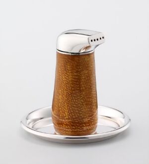  A salt shaker designed by Arne Korsmo named "Pingvin" sits on a reflective silver plate. The shaker features a polished sterling silver cap and an amber-colored enamel-coated conical body displaying a rich caramel hue over a textured surface, embodying a blend of sophistication and practical design.