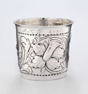  A silver drinking cup, "beger," designed by Albret Groth, with a reflective surface and intricate embossed floral patterns and inscriptions, displaying expert metalwork.