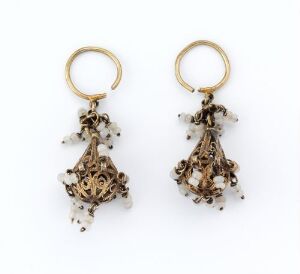  A pair of intricate vintage gold earrings with delicate metal filigree and pale bead embellishments, set against a white background.