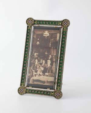  An ornate, dark green and gold framed vintage photograph with a sepia tone, showing a formal gathering, set against a light grey background.