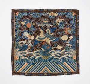  A square traditional textile featuring a mythical phoenix in flight at the center, surrounded by cloud and floral patterns in a palette of deep blue, white, beige, and touches of green and pink, with waves or water patterns in blue and white stripes at the bottom.