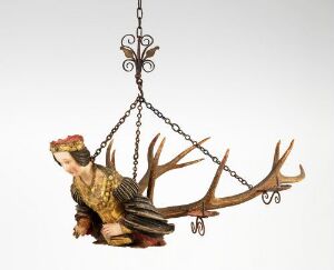  An artistic chandelier titled "Lysekrone" by an unknown artist, featuring a central carved figure from linden wood dressed in yellow and red, seated among symmetrical antler-like branches made of assumed deer horn, with wrought iron detailing for holding candles.