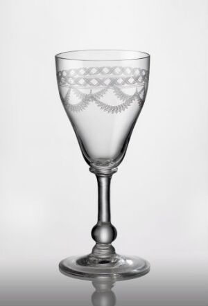  A delicately etched and guilloché patterned glass goblet with a flared bowl set on a slender stem and stable base, displaying intricate symmetrical designs in a transparent and light-reflecting material against a neutral background. Artist unknown.