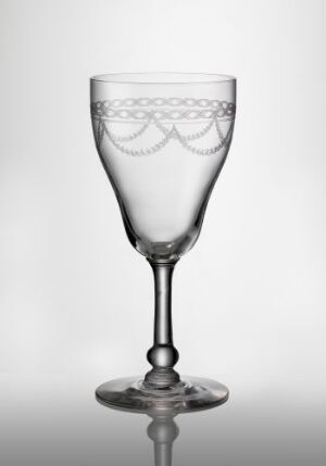  Transparent glass cup with an etched decorative band of interlinking arches and diamonds at the top of the bowl, a short stem, and a flat base, against a gradient gray background. Artist unknown.