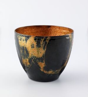  A handcrafted ceramic bowl with a glossy black exterior and an abstract textured gold pattern on one side, paired with a shimmering gold interior, set against a light gray background.