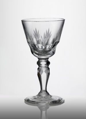 
 An ornate clear glass goblet with detailed faceted, olive, and wheel-cut decorations on the bowl, elegant stem, and sturdy base, set against a light background. Artist name unknown.