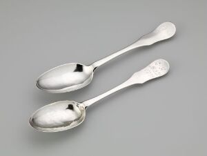  Two silver-colored spoons with reflective surfaces, one with an embossed decorative handle, resting on a light gray background.