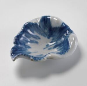  A small, decorative fajanse dish with a white glaze and cobalt blue patterning in a radiating design from the center, featuring scalloped edges shaped like a flower or seashell.