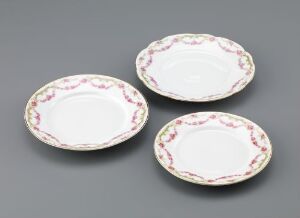  A set of three elegantly crafted feldspar porcelain dishes with printed decorations and gold trim by an unknown artist, arranged against a grey background. One larger plate is set behind two smaller ones, each bordered by a delicate, ornate pattern.