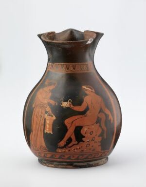  Ancient Greek red-figure vase with a missing handle, featuring a painted scene with two figures, one offering something to the other, set against a deep terracotta background with decorative motifs and patterns on the vase's neck and rim.