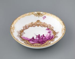  An oval porcelain plate with elaborate gold trim and a central illustration in vivid magenta, depicting a romantic scene set against an off-white background.