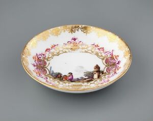  An oval porcelain dish with a white center, ornate gold trim, and a detailed border of multi-colored flowers and a central painted scene depicting figures in historical clothing.