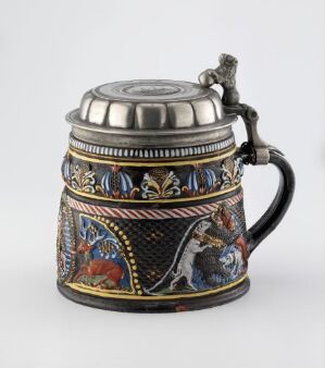  An intricately designed traditional beer stein with a metallic lid and handle, adorned with cobalt blue, gold, and multicolored hand-painted scenes, set against a neutral grey background.