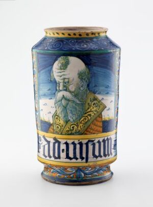 
 A cylindrical ceramic vase with a rich blue and gold design, featuring a Greek key pattern at the top and bottom, and a central painted portrait of a person in profile, wearing elaborate historical attire.