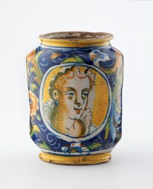  An ornate ceramic apothecary jar, with a central cobalt blue background featuring a profile of a woman in a white and golden-yellow medallion, surrounded by stylized acanthus leaves and scroll patterns.