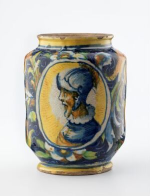  A ceramic vase with a classical figure's profile in cobalt blue on a golden-yellow oval medallion, surrounded by blue and yellow leafy motifs, against a light background.