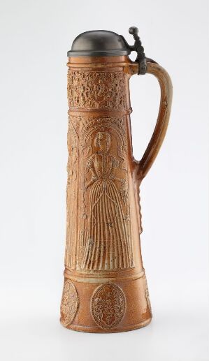  A tall, cylindrical stoneware stein with a warm tan color and darker relief decorations, designed by Jan Emens Mennicken and titled "Judith, Ester, Johannes og Lukas." It features embossed figures surrounded by decorative motifs, a gracefully curved handle and a fitted pewter lid on top, set against a white background.