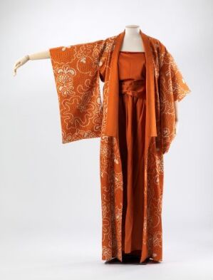  A traditional orange robe with an intricate floral pattern draped elegantly on a mannequin against a light gray background.