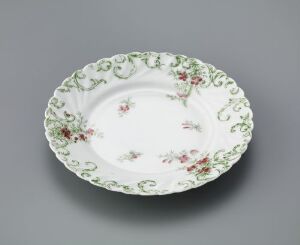  An image of a traditional feldspar porcelain plate titled "Modell 1111" by an unknown artist. It showcases a white background with a pale green decorative border and hand-colored floral motifs in pink and red hues.