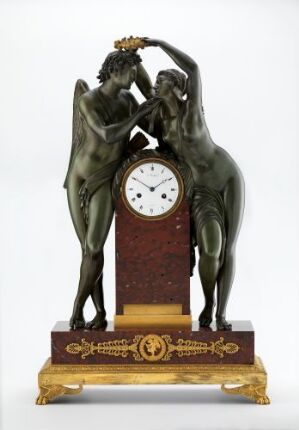  An intricate bronze sculptural clock featuring a dancing male and female figure entwined around a central clock with a white face and Roman numerals, set against a red-brown panel on a gilded decorative base.