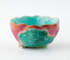  A small ceramic or porcelain bowl designed to mimic a flowering bloom, featuring a bright turquoise interior transitioning to coral pink edges with leaf-life textures and delicate green supporting feet.