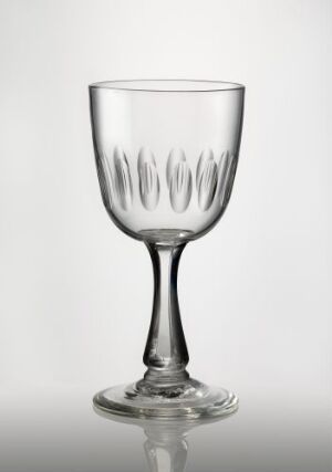  A clear blown glass goblet with facet and olive cuts decorating the lower part of its bell-shaped bowl, a slender stem, and a flat base, against a light neutral background. Artist and title are unknown.