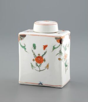  A porcelain tea caddy with a white base and colorful hand-painted floral decorations, featuring a rectangular body and a cylindrical neck with a fitted lid.