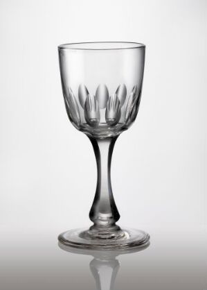  A clear blown glass goblet with faceted and olive-cut pattern, on a light grey background. The artist is unknown. The glass has a narrow stem and a solid base, and the body features an elegant petal-like design. The image exemplifies fine glassware craftsmanship.