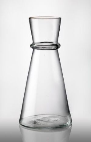  A clear, colorless, blown glass container with a conical shape and a flared opening, featuring a decorative ring at the neck, displayed against a white background. Artist is unknown.