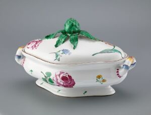  An oval porcelain serving dish with a lid, featuring a glossy white background adorned with hand-painted floral designs in pinks, reds, yellows, blues, and purples, and a prominent green artichoke-shaped handle on the lid.