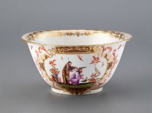  An ornate porcelain bowl with a creamy white background featuring a detailed scene with human figures in an Asian landscape on a central cartouche, surrounded by floral motifs and gold scrollwork, with a gold-trimmed rim. Artist name and title are unknown.