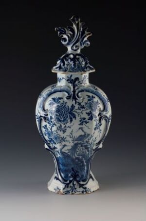  A traditional blue and white porcelain vase with a bulbous body, narrow neck, and flared base, featuring intricate cobalt blue floral patterns and baroque style flourishes against a white background. The vase has ornate handles and a matching lid with a decorative finial.