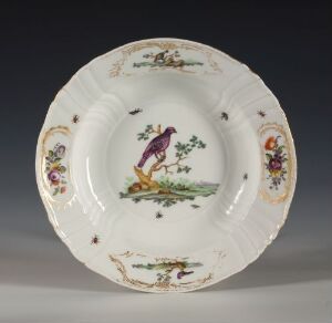  An exquisitely detailed porcelain plate from Den kgl. Porcelainsfabrik with a central painting of a purple bird on a branch, surrounded by colorful floral designs with gold accentuations on a white background.