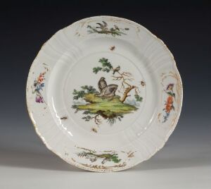  A porcelain plate from Den kgl. Porcelainsfabrik featuring a scalloped edge, with a central image of a bird amidst greenery, surrounded by smaller pastoral scenes, all rendered with vivid overglaze decoration.