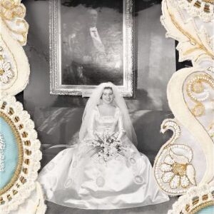  A black and white photograph of a bride in a traditional wedding dress centered within a decorative frame with white, cream, and gold baroque elements.