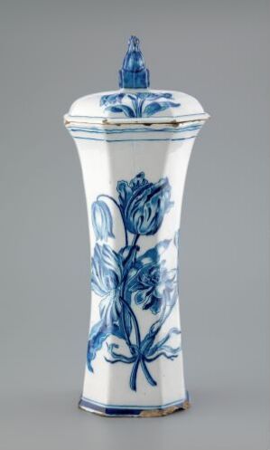  A tall white porcelain mustard pot with intricate cobalt blue floral designs, narrowing at the neck and topped with a lid that has a small, dark blue ornate handle.