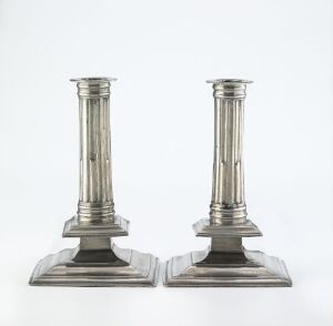  A pair of squared-base pewter candlesticks with cylindrical shafts featuring horizontal grooves, designed by Hugh Quick and entitled "To Lysestaker," against a white background. The metal has a soft silvery-gray sheen, and the craftsmanship showcases both casting and soldering techniques with chiseled details.