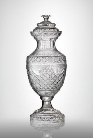  An elegant, transparent glass vase with a removable lid, featuring intricate patterns and diamond cuts, against a soft gray gradient background.