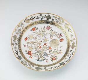  Decorative plate with scalloped edges and gold trim featuring a central floral design in shades of pink, orange, yellow, and green, with additional floral and foliage accents around the perimeter against a creamy white background. Artist and title are unknown.